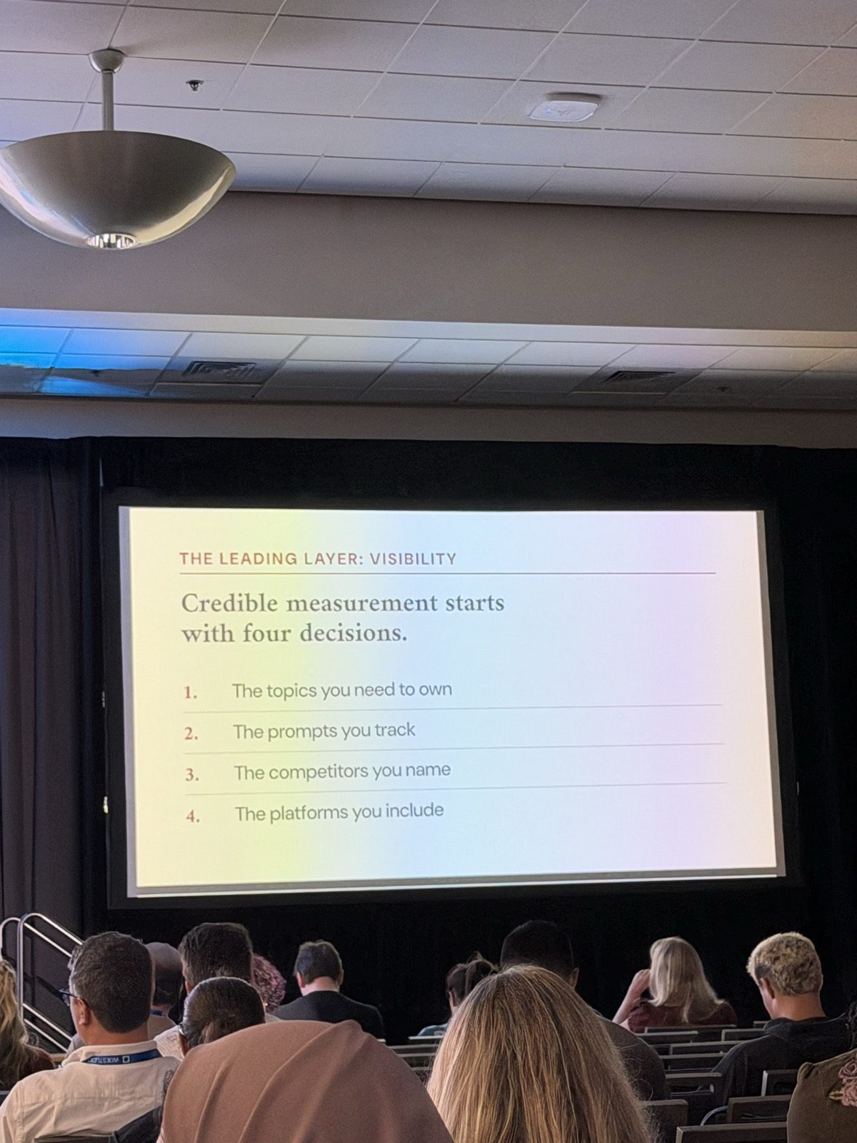 Slide 'The leading layer: visibility. Credible measurement starts with four decisions': 1. The topics you need to own; 2. The prompts you track; 3. The competitors you name; 4. The platforms you include.